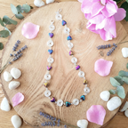 Necklace with colorful beads on a wooden surface with flowers and stones