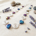 Necklace with heart-shaped beads and silver spirals on a textured surface with lavender flowers and stones