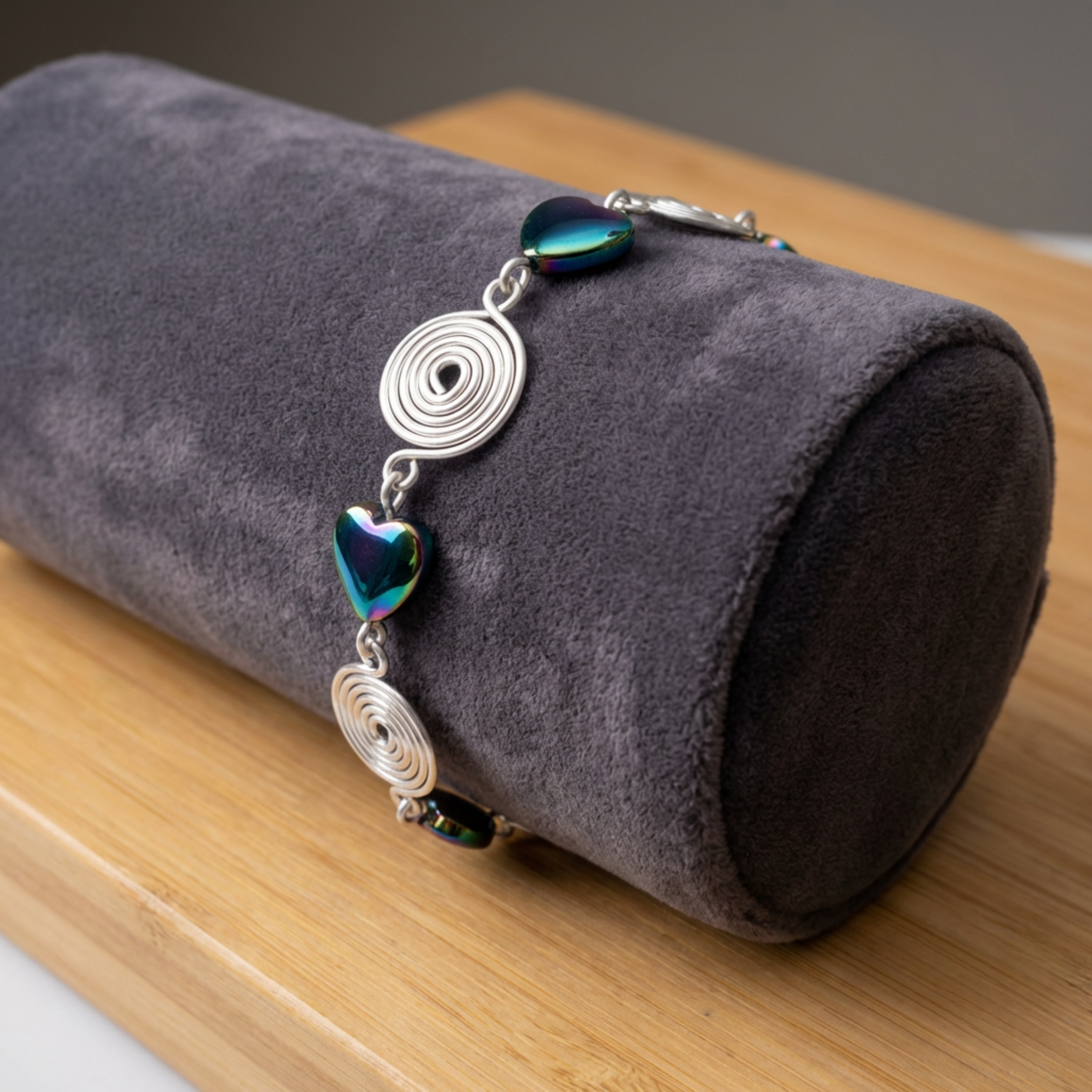 Bracelet with heart and circular designs on a grey cylindrical pillow against a wooden surface.