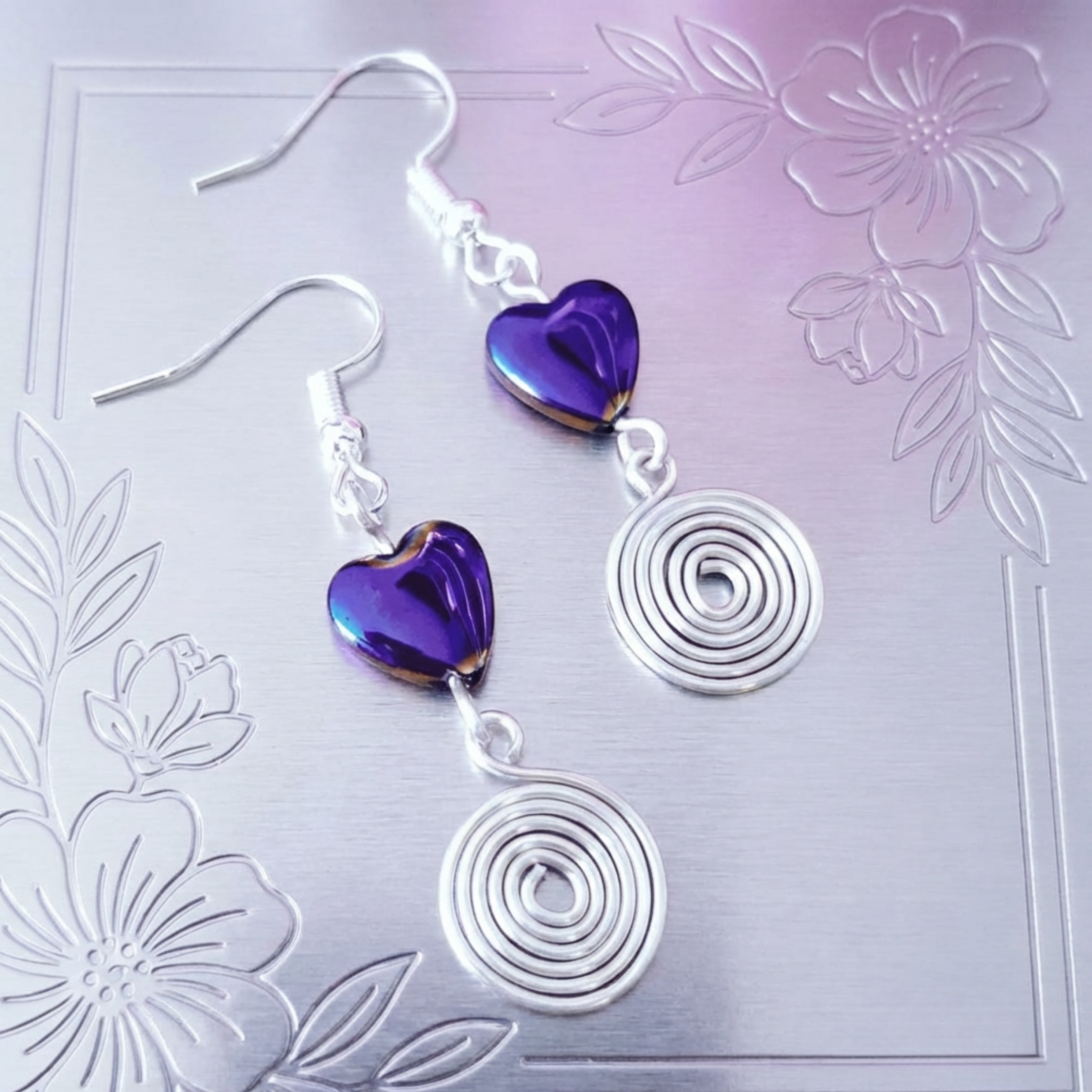 Purple heart-shaped earrings with silver spiral designs on a floral background