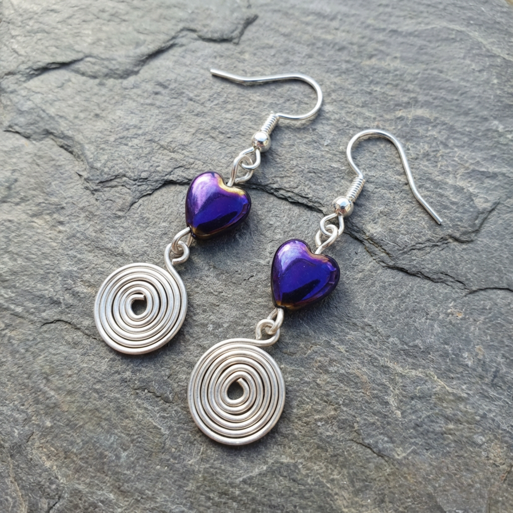 Silver earrings with purple heart-shaped beads on a stone surface