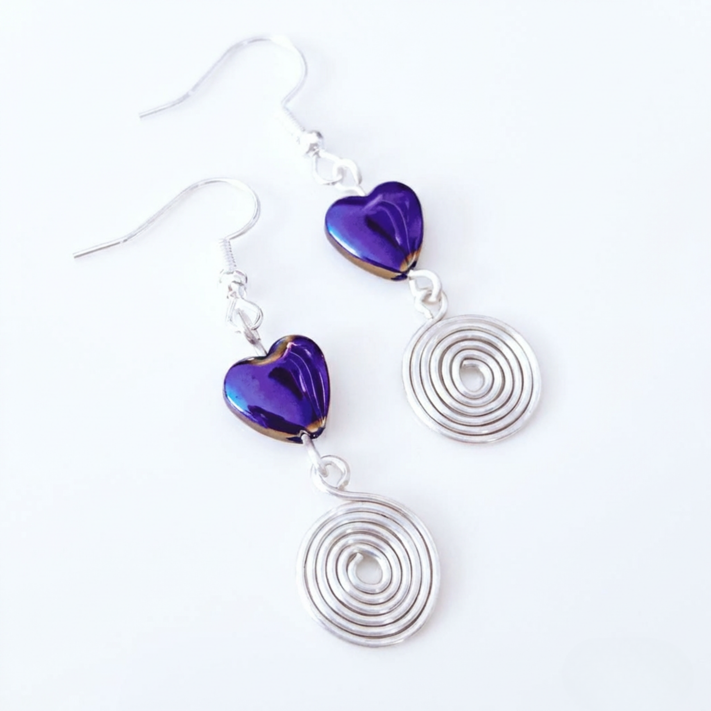 Earrings with purple heart-shaped beads and silver spiral designs on a white background