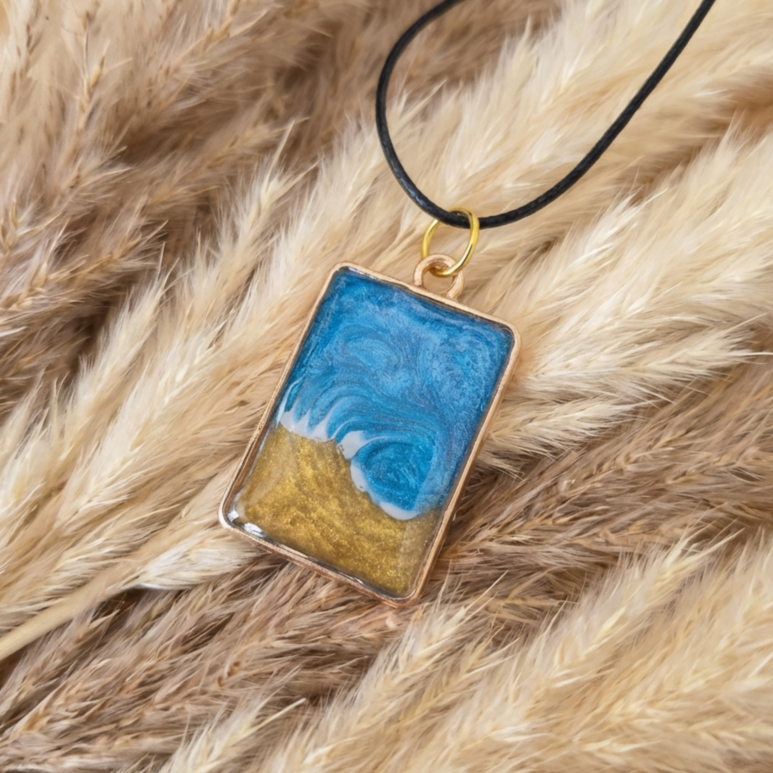 Rectangular pendant with blue and gold design on a black cord, lying on fur.
