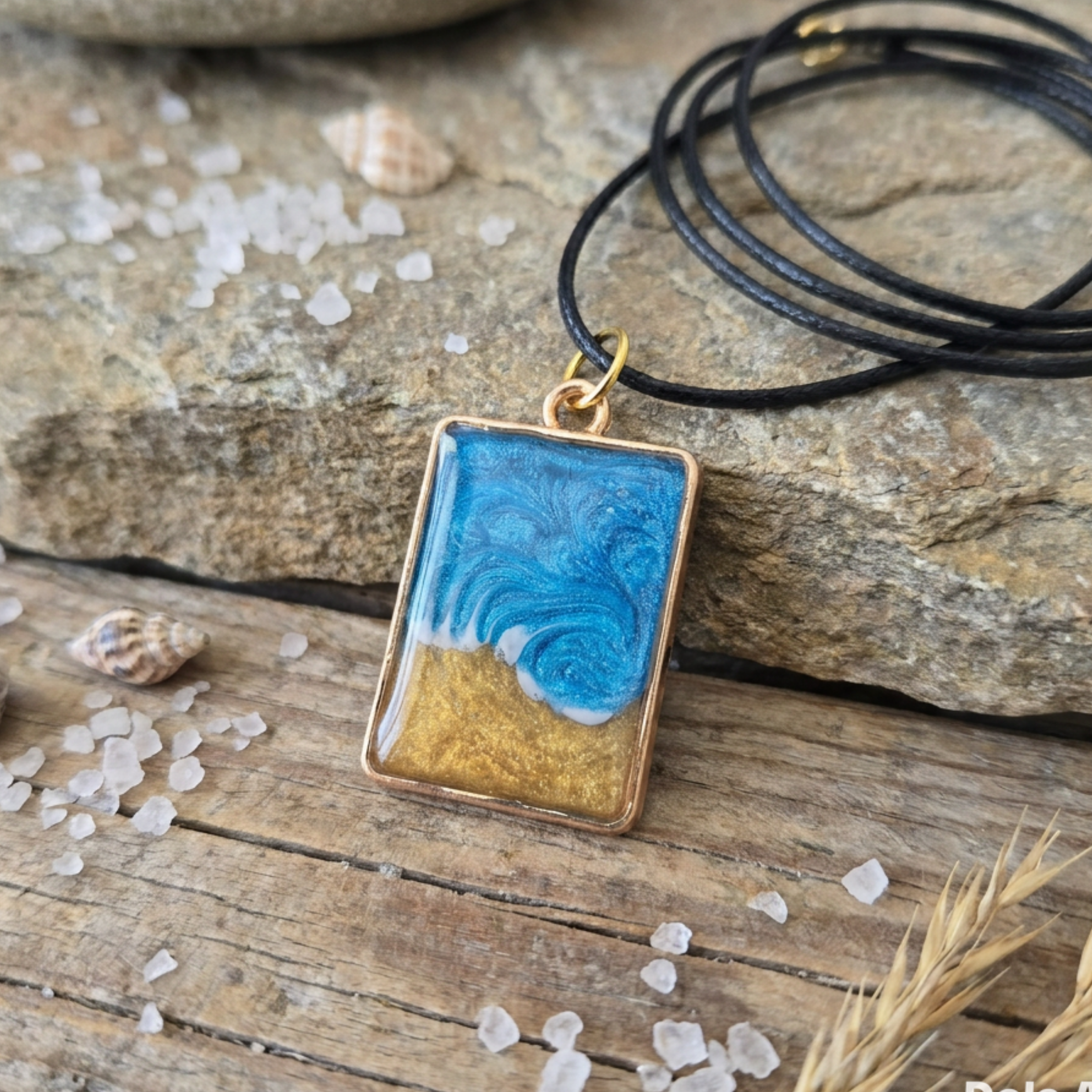 Gold Bezel seascape wave pendant on a black cord on stone and wood surface