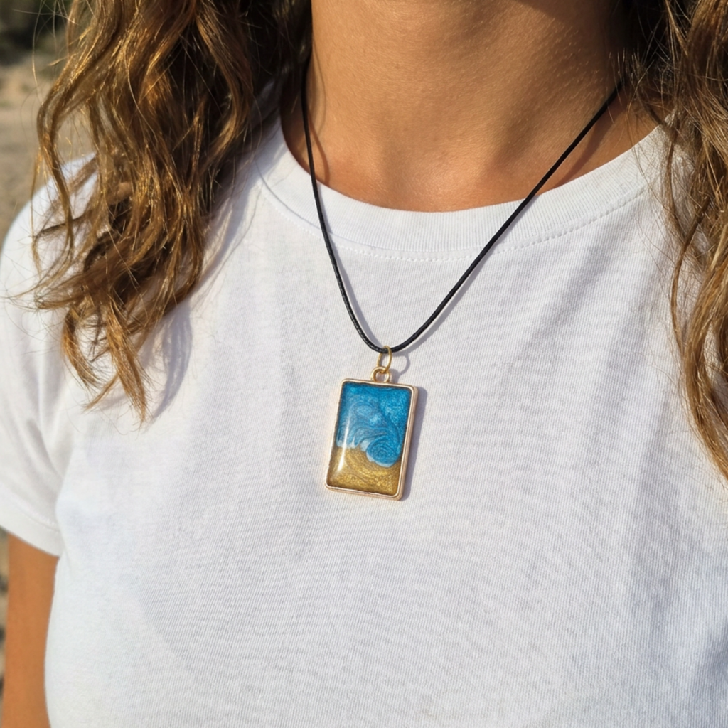 Person wearing a necklace with a pendant featuring a beach scene on a white shirt.