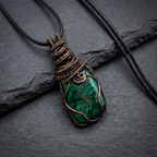 Green stone pendant with copper wire wrapping on a dark surface