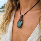 Necklace with a green pendant worn by a person on a beach.