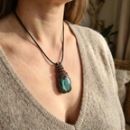 Necklace with a green pendant worn by a person in a beige sweater.