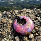 Donut shaped pendant with pink purple and gold colours on a black cord