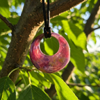 Pink woven ring hanging from a tree branch with green leaves in the background