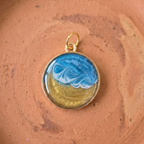 A gold round pendant with a wave effect on a stone surface