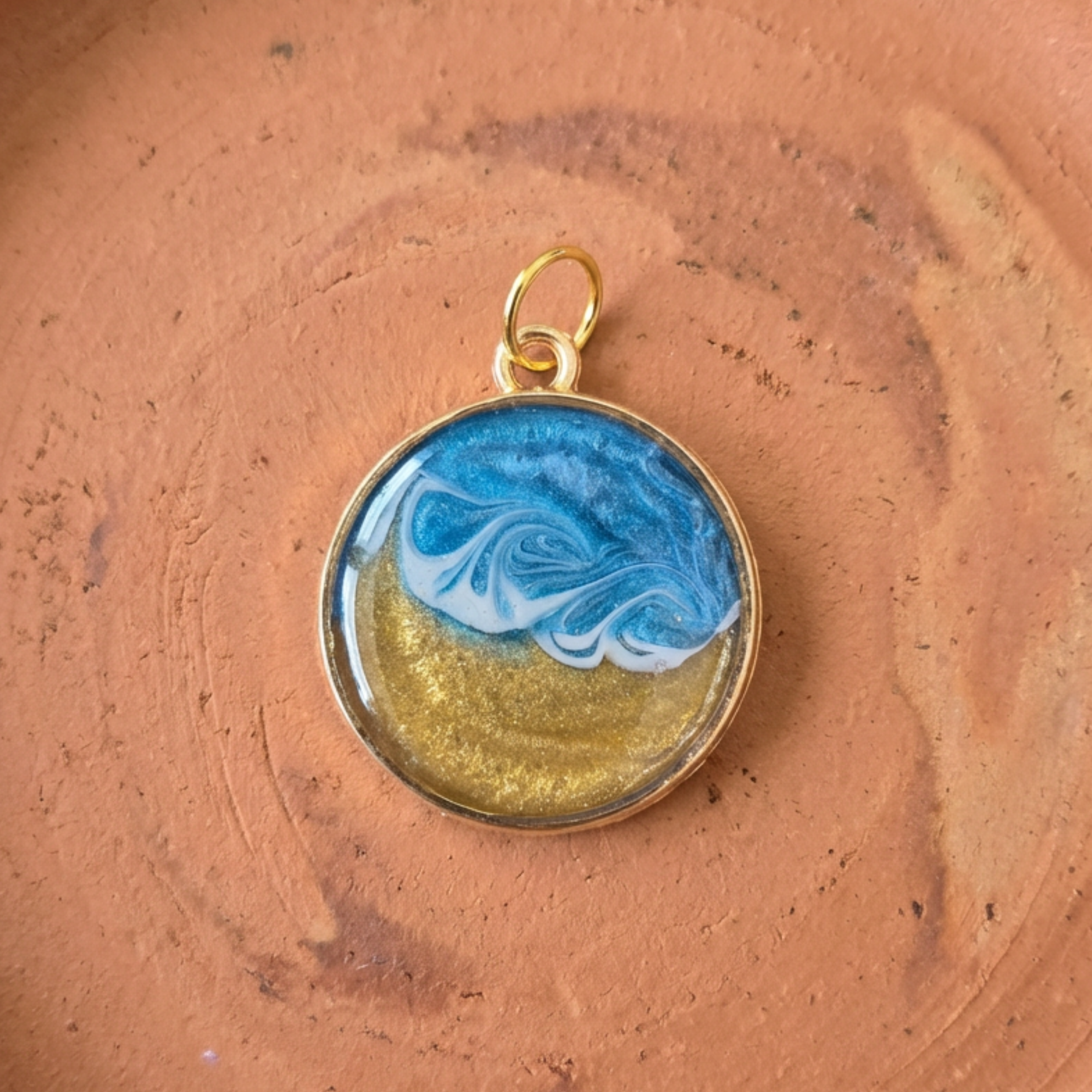 A gold round pendant with a wave effect on a stone surface