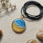 Pendant with a wave design in a gold bezel on a black cord on a fabric surface