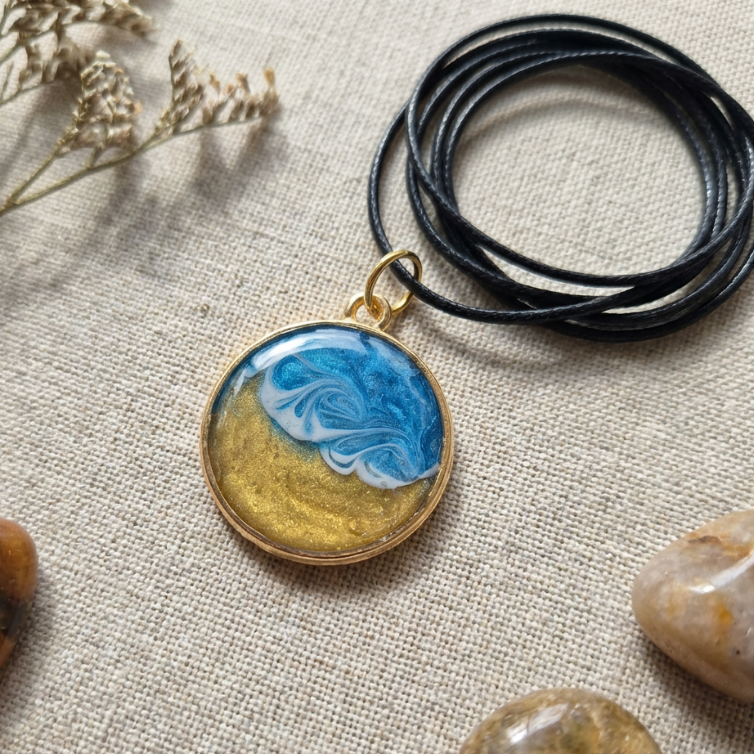 Pendant with a wave design in a gold bezel on a black cord on a fabric surface