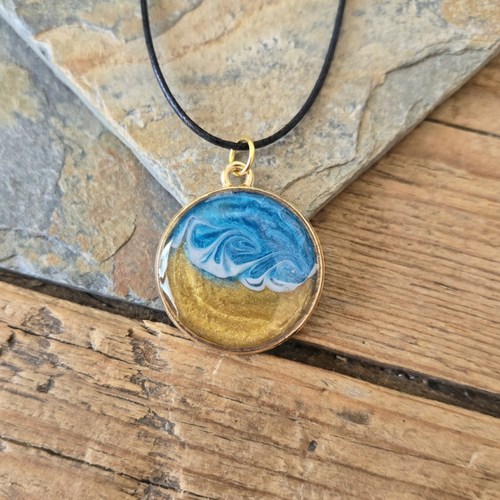 Necklace with a pendant featuring blue and gold design on a wooden surface
