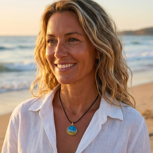 woman wearing a gold round pendant with a wave design on a beach