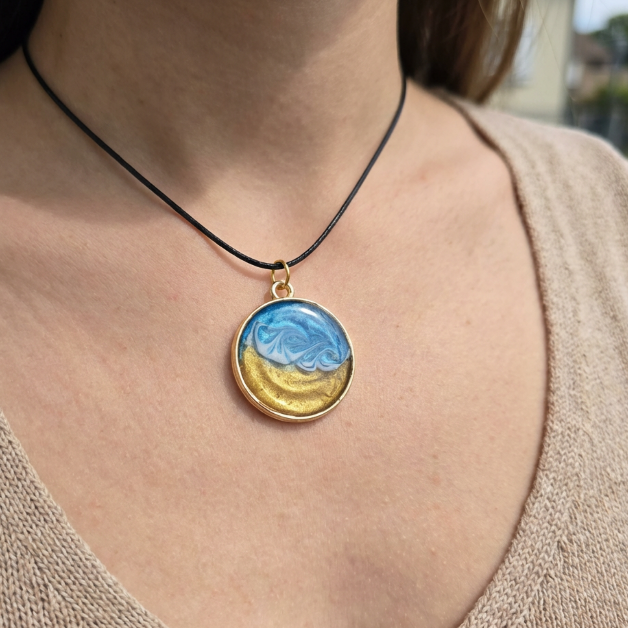 Person wearing a necklace with a round pendant featuring blue and yellow colors.