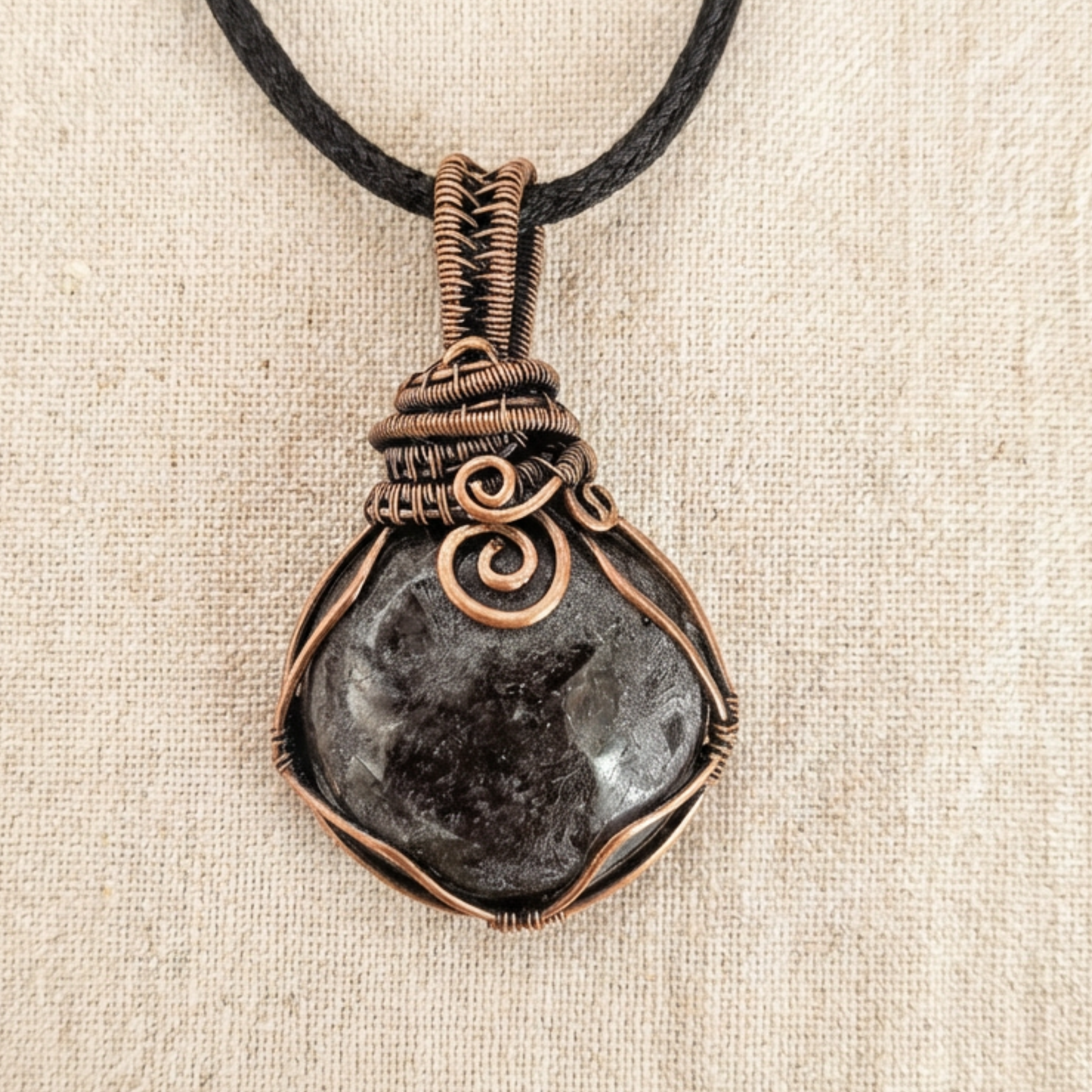 Necklace with a dark stone pendant and copper wire wrapping on a beige fabric background