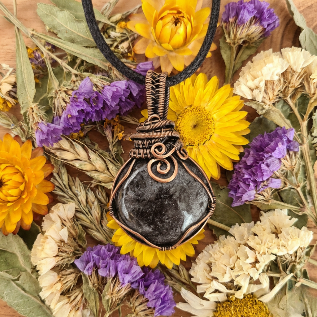 Necklace with a black stone pendant surrounded by dried flowers on a wooden surface