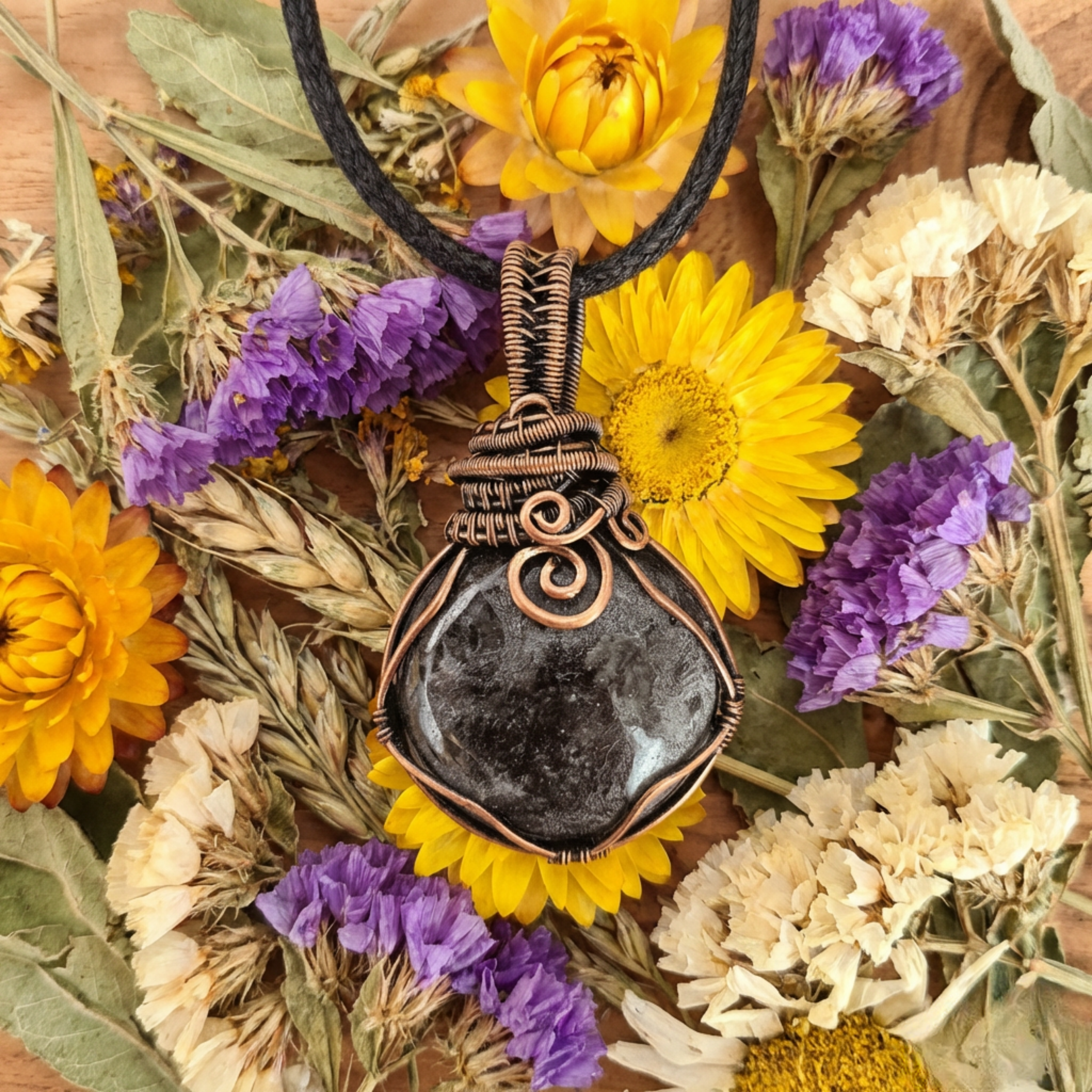 Necklace with a black stone pendant surrounded by dried flowers on a wooden surface