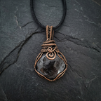 Necklace with a dark stone pendant and copper wire wrapping on a black stone background