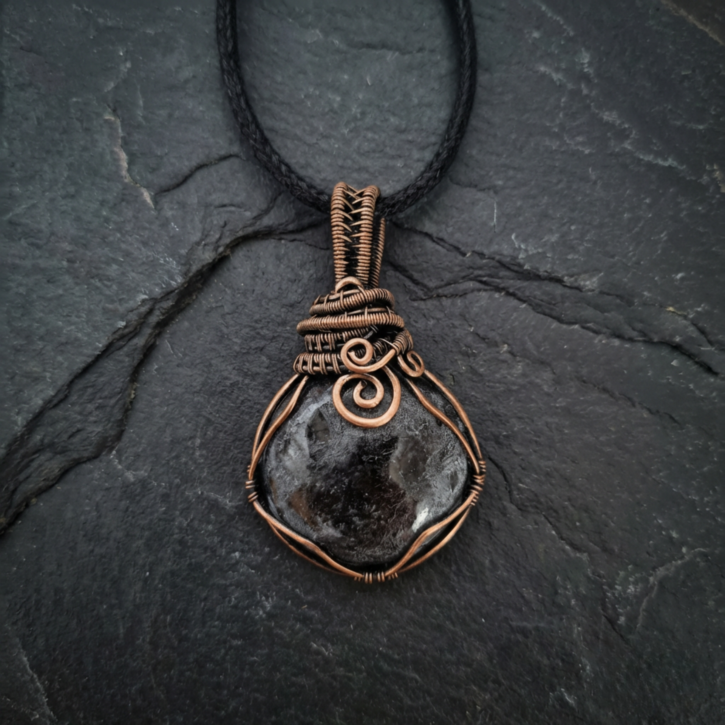 Necklace with a dark stone pendant and copper wire wrapping on a black stone background