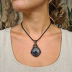 Person wearing a necklace with a dark green labradorite pendant and bronze wire wrapping, outdoors.