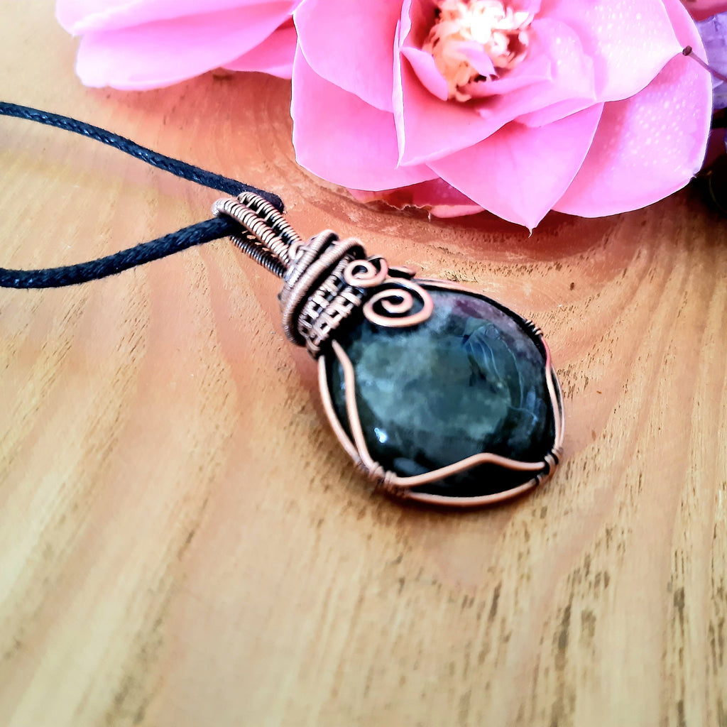A simple labradorite copper wire wrapped pendant on a wooden surface with pink flowers