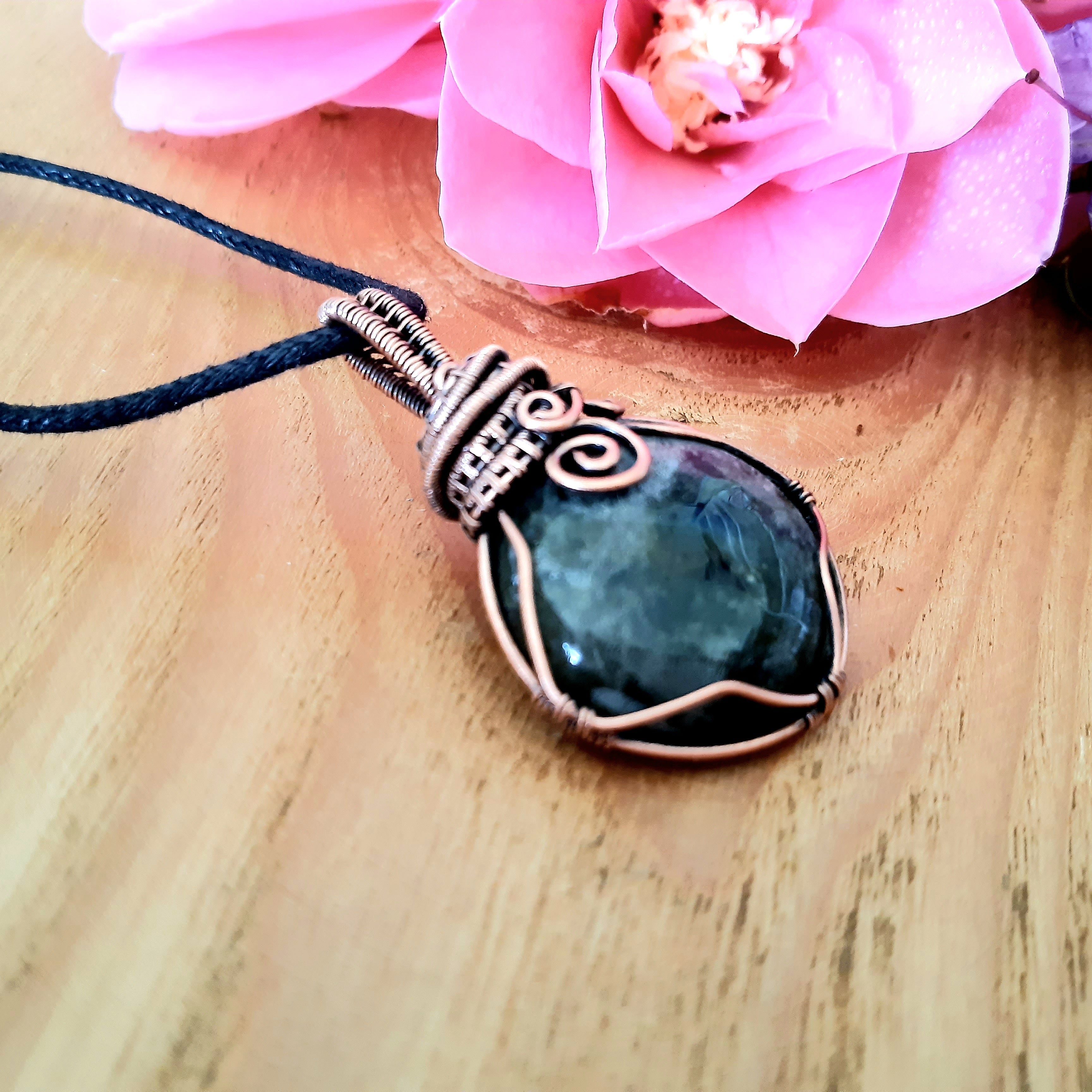 A simple labradorite copper wire wrapped pendant on a wooden surface with pink flowers