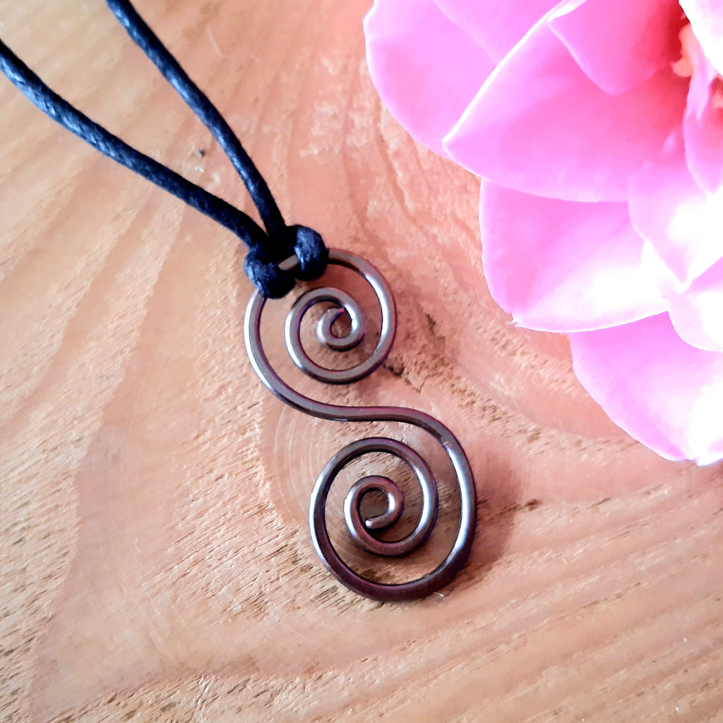 Metallic copper spiral pendant on a black cord with pink flowers on a wooden surface