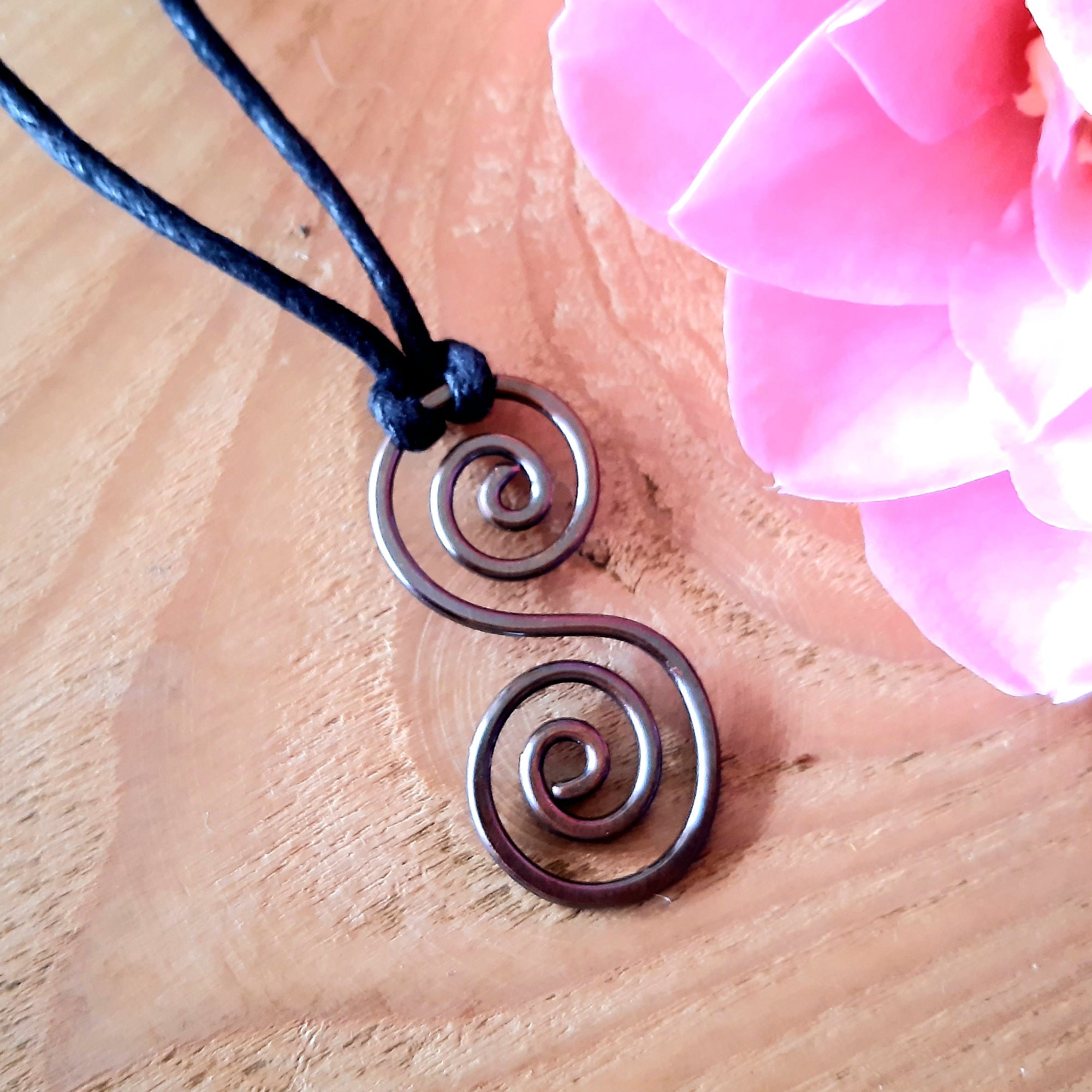 Metallic copper spiral pendant on a black cord with pink flowers on a wooden surface