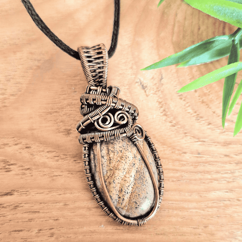 Necklace with a stone pendant on a wooden surface with a leaf in the background
