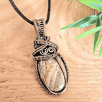 Necklace with a stone pendant on a wooden surface with a leaf in the background