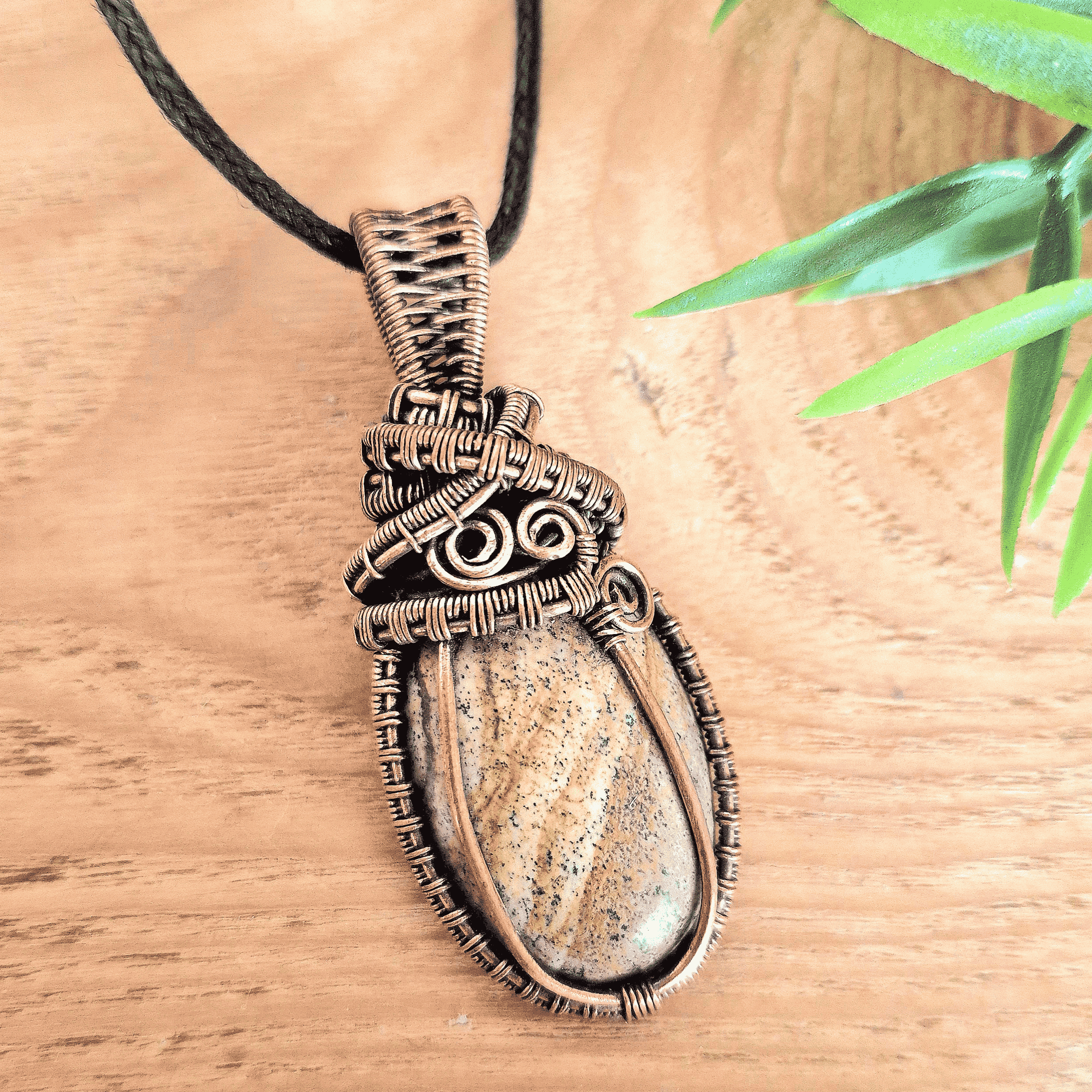 Necklace with a stone pendant on a wooden surface with a leaf in the background