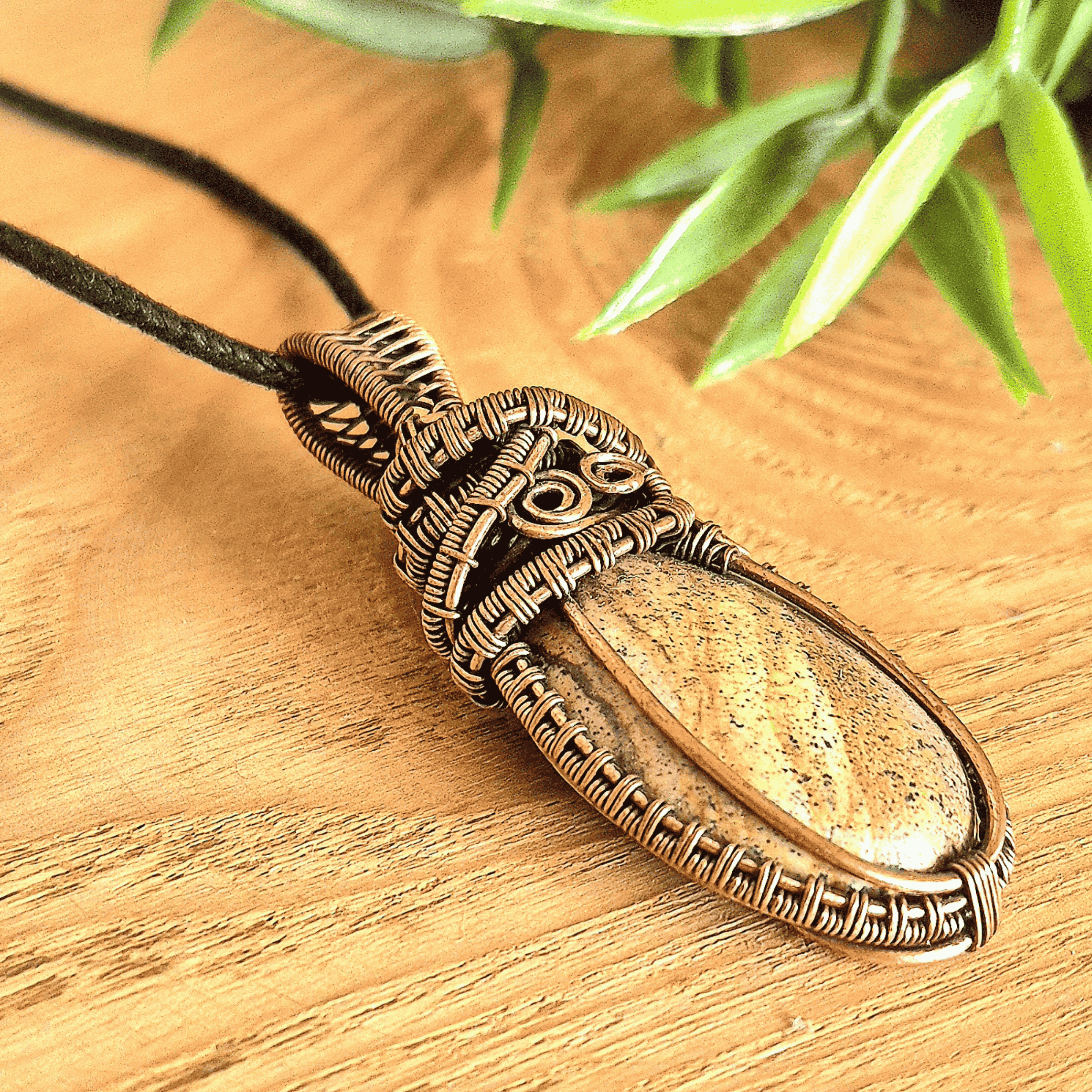 Bronze pendant with a stone on a wooden surface with green leaves in the background