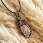 Bronzed copper wire-wrapped pendant with a stone on a fluffy beige surface