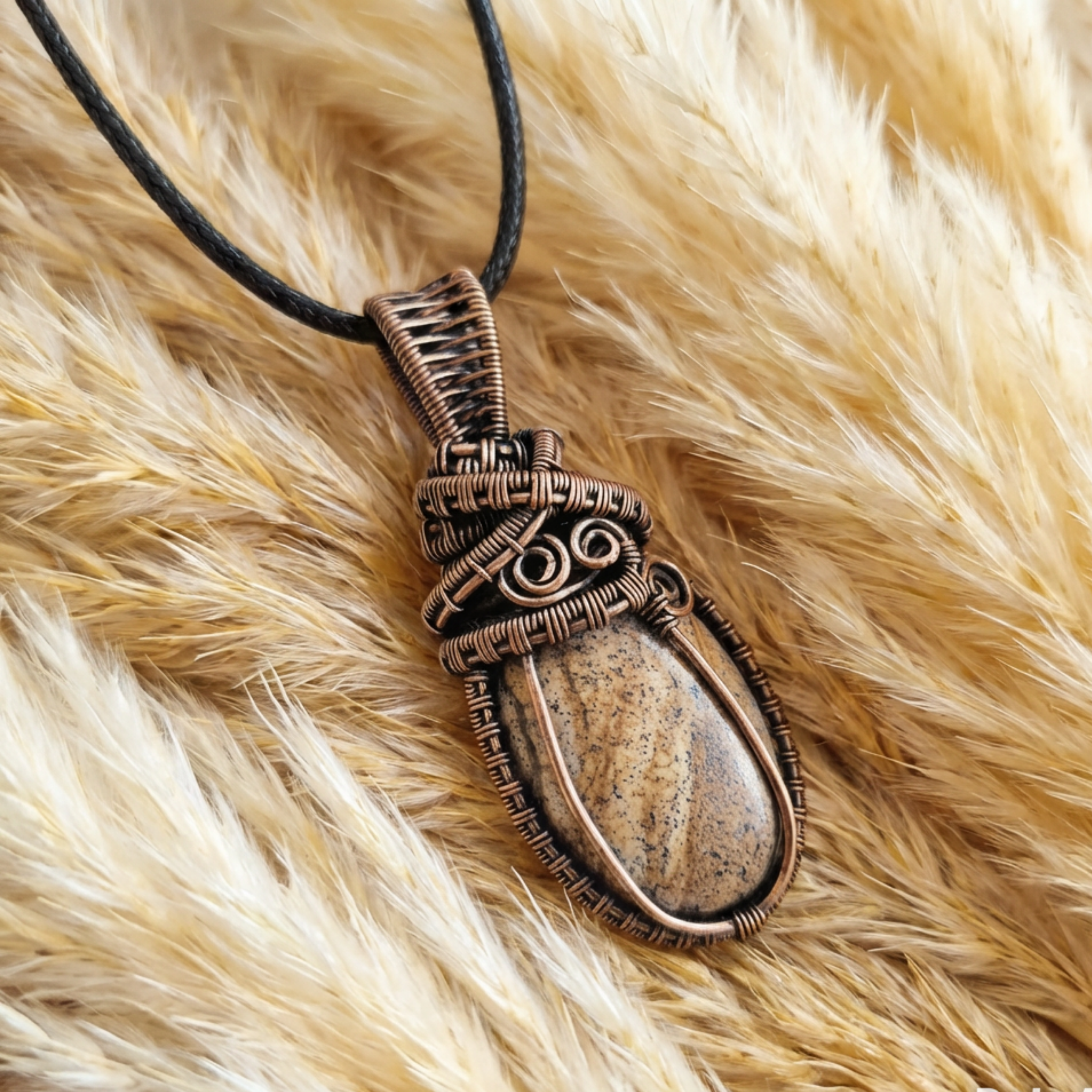 Bronzed copper wire-wrapped pendant with a stone on a fluffy beige surface