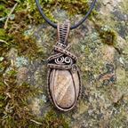 Copper wire-wrapped pendant with a stone on a mossy rock background