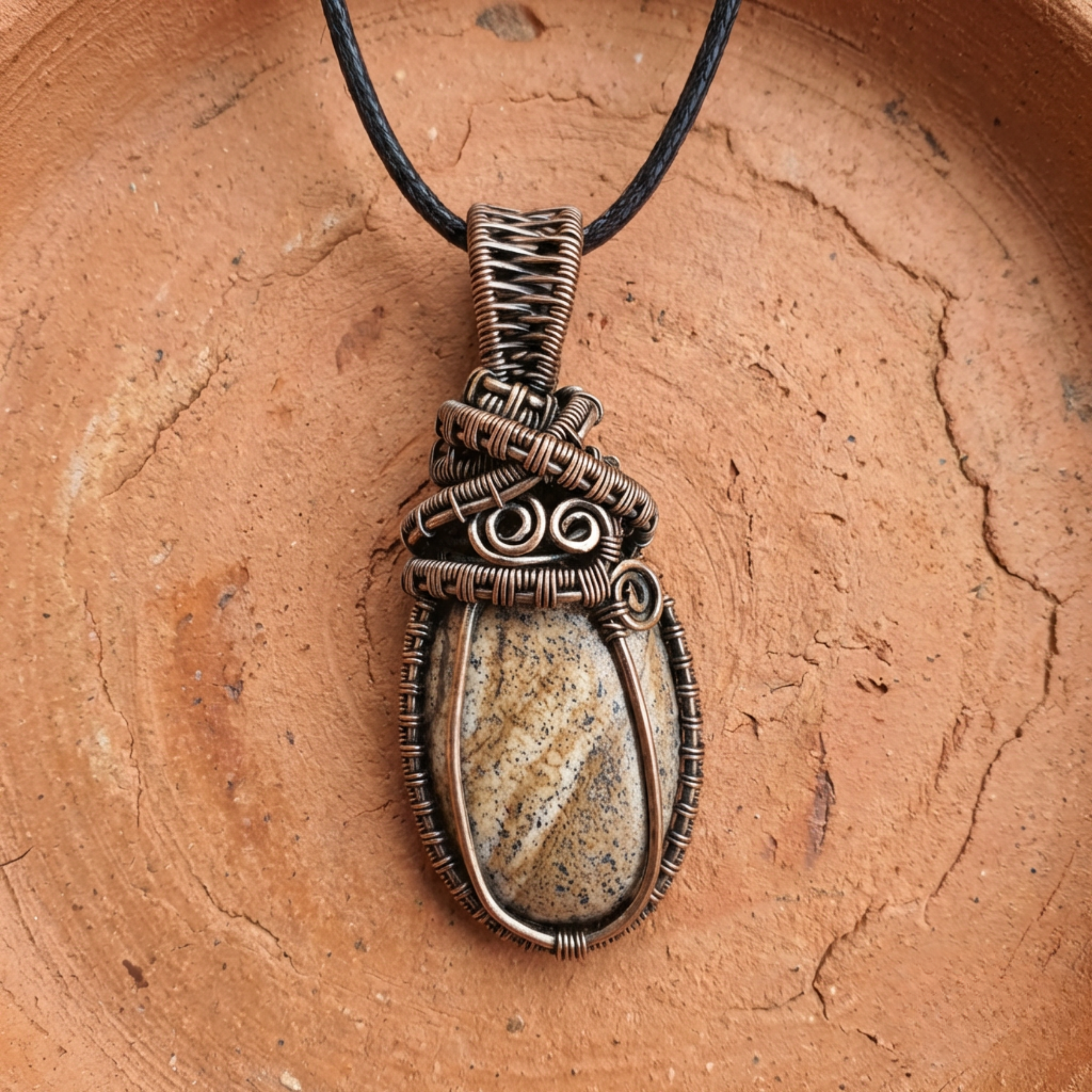 Bronze wire-wrapped pendant with a stone on a brown surface