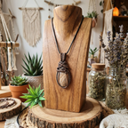 Wooden necklace display with a pendant on a wooden stand, surrounded by plants and jars.