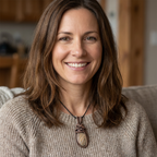 Woman wearing a beige sweater with a necklace, sitting on a couch.