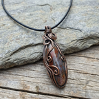 Copper wire-wrapped gemstone pendant on a black cord against a stone background