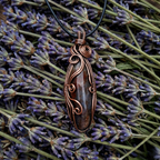 Copper wire-wrapped pendant on a black cord with lavender flowers in the background