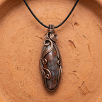 Copper pendant with stone on a black cord against a terracotta background