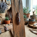 Decorative pendant necklace on a wooden stand with potted plants in the background
