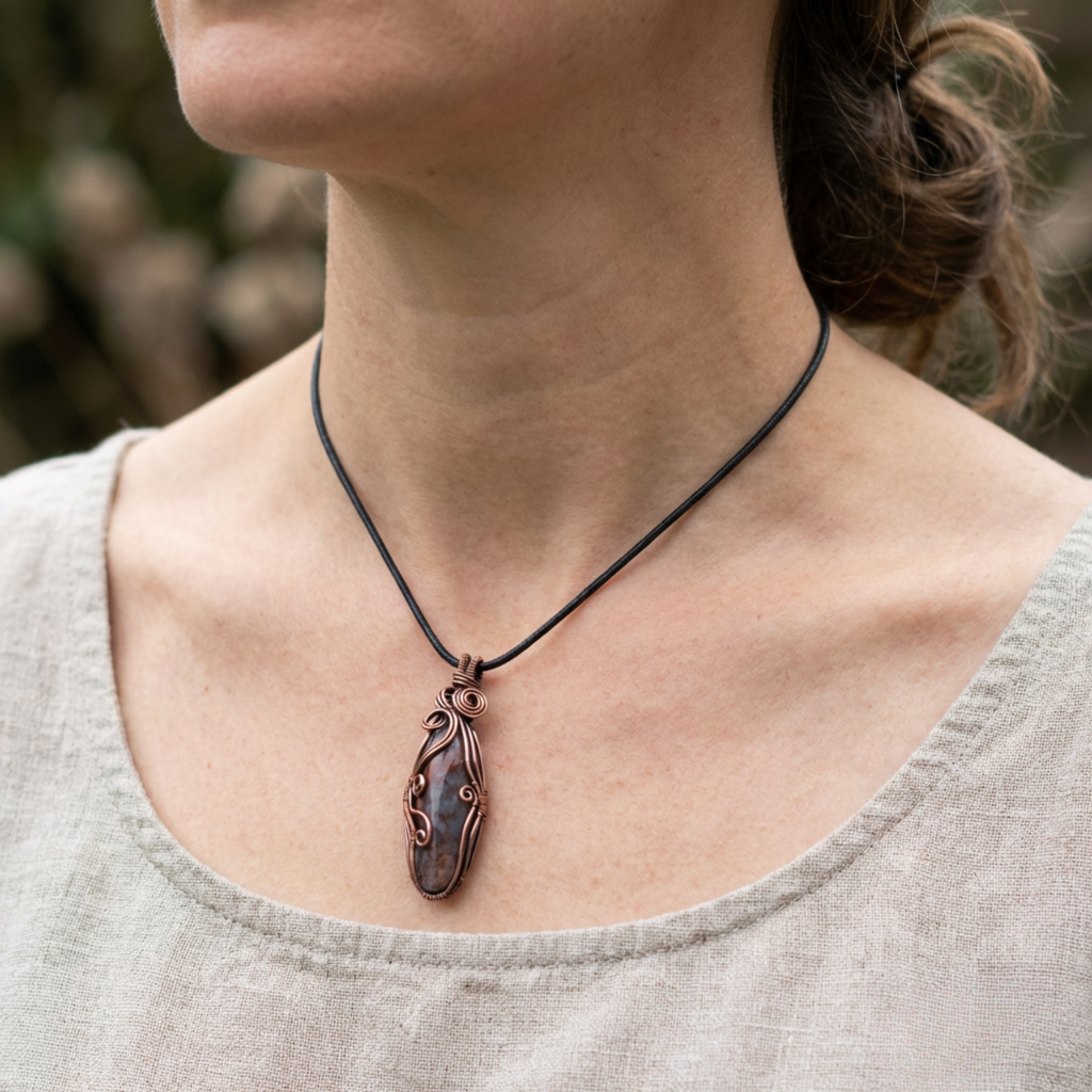 Person wearing a necklace with a copper and gemstonependant against a blurred natural background