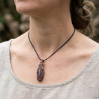 Person wearing a necklace with a copper and gemstonependant against a blurred natural background