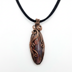 Copper-wrapped pendant with a Seftonite stone on a black cord against a white background