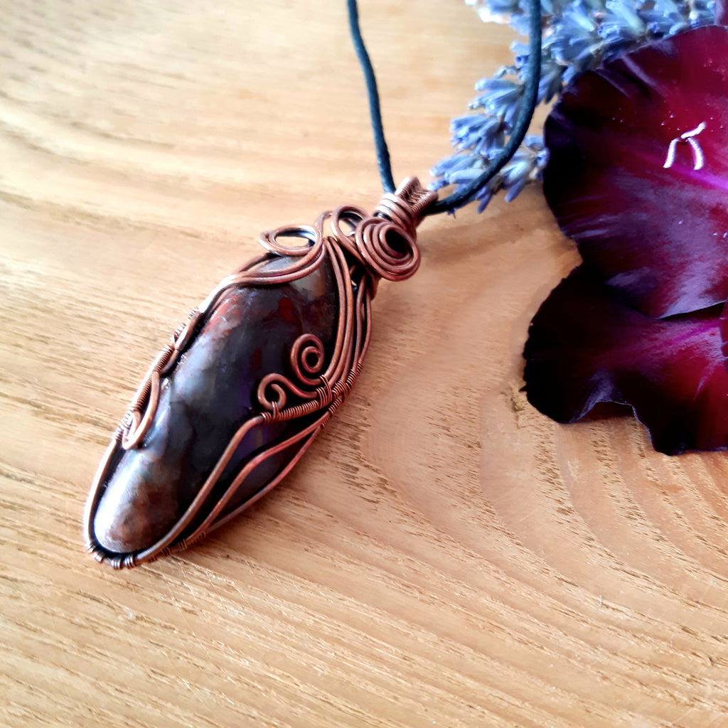 Copper Seftonite gemstone pendant on a wooden surface with a purple flower