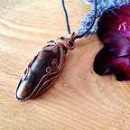 Copper Seftonite gemstone pendant on a wooden surface with a purple flower